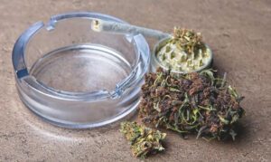 Hemp flower next to a grinder, a glass ashtray, and a joint