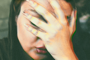 A woman with her eyes closed and hand on forehead in discomfort, appearing to have nausea or a headache