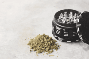 Dry kief sits in a pile next to a black weed grinder