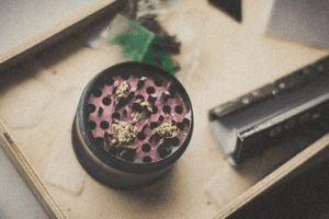 A purple weed grinder filled with a little bit of weed sits next to rolling papers on a table