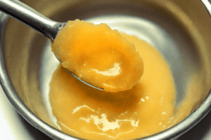 Close up shot of a tiny spoon scooping some cannabis butter out of a metal tray.