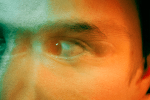 Frightened man with fearful expression, eyes wide in distress, surrounded by green and orange lights