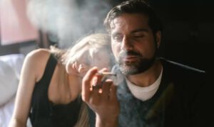 Man and woman smoke a joint while sitting in bed.